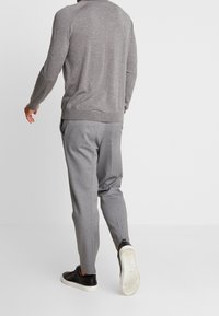 Szary sweter o dopasowanym kroju, w zestawieniu z jasnoszarymi spodniami typu tapered. Czarne sneakersy z białymi podeszwami. Prosty, minimalistyczny wygląd.