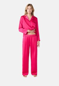 Roze satijnen pyjamastel met een button-up shirt met een zak en lange mouwen, gecombineerd met losse, recht gesneden broek.