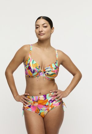 Vrouw met donker haar in een bloemenprint multikleurige bikini met hoge taillebroek, staand met handen in de zij tegen een effen witte achtergrond.