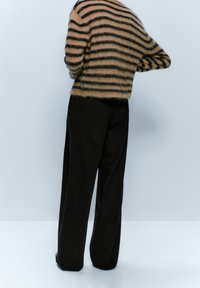 Pull en laine fuzzy rayé marron et noir au design court associé à un pantalon noir ample. La texture semble douce et chaude.