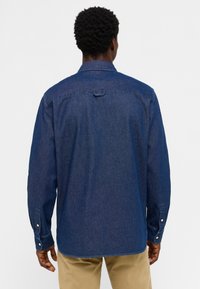 Ciemnoniebieska koszula dżinsowa z długimi rękawami, kołnierzykiem, zapięciem na guziki przy mankietach oraz prostym krojem. Posiada karczek z tyłu i wykończone brzegi.