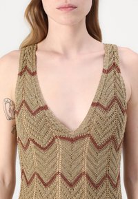 Top in maglia metallizzato dorato con scollatura a V profonda. Caratterizzato da un motivo a zigzag con accenti bordeaux. Tessuto testurizzato con un design a trama larga.