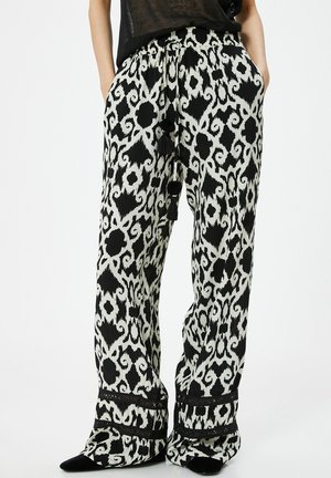 Wijdvallende broek met een zwart-wit dierenprint, voorzien van een koordtaille en zwarte franjes, gemaakt van lichte stof.