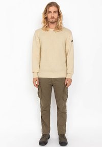 Beige gebreide trui met textuur en een ronde hals, gecombineerd met olijfgroene cargobroek met zijzakken en aangesloten boorden.