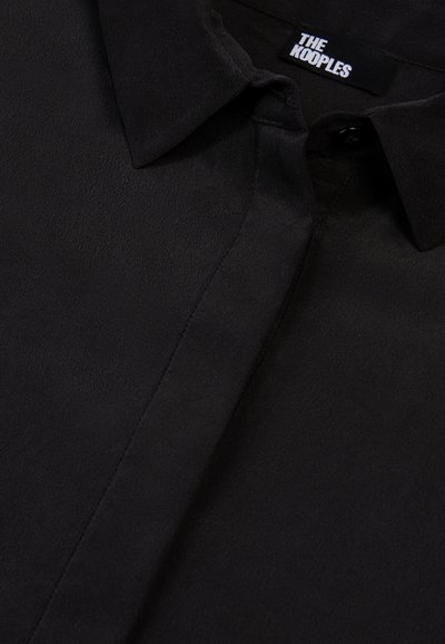 Zwarte blouse met kraag van soepel materiaal, voorzien van een knoopsluiting aan de voorkant en het etiket van The Kooples zichtbaar bij de hals. Zachte textuur, geen patronen.