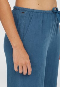 Blue, textured, mid-rise pants made of soft, breathable material with an adjustable waistband and side pockets. Includes a small brand tag.