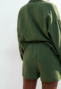 Conjunto de camisa y pantalones cortos de lino verde. Parte superior holgada con cuello, cinturilla elástica en los pantalones cortos, tela texturada con un ligero brillo.