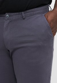 Grå chinos laget av et glatt stoff, med slim fit, sidelommer og knappestenging. Diskret diagonalt vevemønster.
