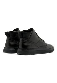Paire de bottines en cuir noir à surface texturée, avec lacets à l'avant, col rembourré et semelles épaisses en caoutchouc, vues de l'arrière en angle latéral.