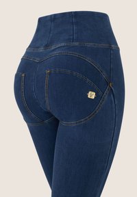 Jeans de mezclilla oscuros de talle alto con costuras en contraste, bolsillos traseros curvados y un pequeño acento metálico cerca del bolsillo.