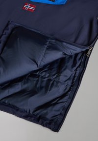 Marinejas met blauwe accenten, voorzien van een ritszak en een geborduurde vlag. Glad buitenmateriaal met een gevoerde binnenvoering.