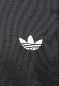 Μαύρο πλεγμένο ύφασμα με λευκό κεντημένο λογότυπο Adidas trefoil και τρεις ρίγες κάτω από το σχέδιο. Υφή με ορατές τρύπες.