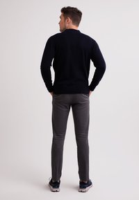 Námořnický pletený svetr s žebrovaným límcem, spárovaný s šedými slim-fit kalhotami a tmavými teniskami, viděný zezadu.