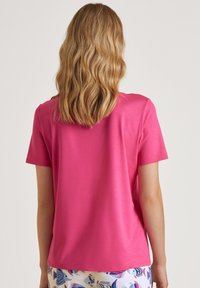 Korte mouwen, ronde hals t-shirt in levendig roze stof. Soepele textuur, relaxte pasvorm, gezien van de achterkant, gecombineerd met een patroonshort.