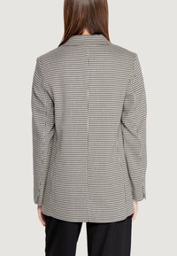 Blazer in un motivo a scacchi bianco e nero, con spalle strutturate, una fessura singola, maniche lunghe e una texture di tessuto liscia.