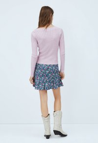 Light pink ribbed sweater with long sleeves, paired with a floral-patterned, knee-length skirt featuring blue, pink, and green hues.