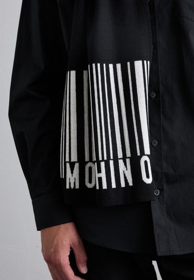 Svart strikket skjerf med hvite vertikale striper og teksten "MOHINO" nederst. Myk tekstur, rektangulær form, uformell design.