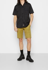 Černé tričko s krátkým rukávem a dvěma kapsami na prsou, spárované s khaki kraťasy a černými teniskami. Texturovaná látka s volným střihem.