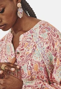 Blusa de tejido suave con estampado floral, presenta tonos de rosa, azul y amarillo. Detallada con bordado a lo largo de la costura del hombro y un cierre de botones en el frente.