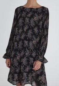 Svart tygklänning med blommönster i nyanser av blått, rosa och kräm. Har långa ärmar, plisserad textur och volangkant.