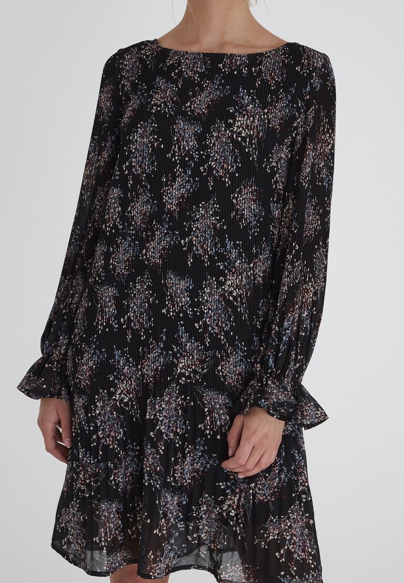 Svart tygklänning med blommönster i nyanser av blått, rosa och kräm. Har långa ärmar, plisserad textur och volangkant.