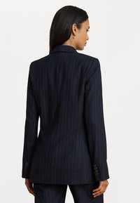 Marineblauwe pinstriped blazer met een tailored fit, gestructureerde schouders en knoopmanchetten. Gelijke textuur en ontwerp van middellange lengte.