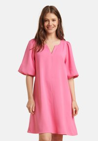 Rosa Kurzarmkleid mit V-Ausschnitt und Puffärmeln. Der Stoff wirkt glatt; Die A-Linie sorgt für eine fließende Silhouette.