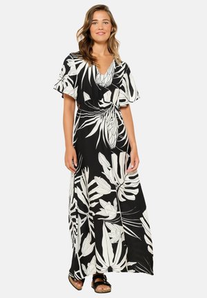 Schwarzes Maxikleid mit weißem tropischem Blattmuster, kurzen, schwingenden Ärmeln, V-Ausschnitt und tailliertem Bund. Getragen mit schwarzen Sandalen.
