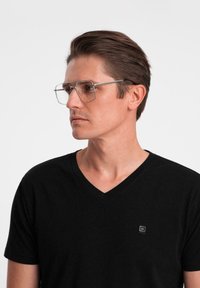 Klart rektangulära glasögon har en tunn metallram. Bärs av en person i en svart V-ringad tröja. Ren, minimalistisk design utan utsmyckningar.