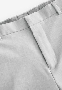 Pantalon gris clair en tissu lisse, avec un devant plat, des coutures latérales et une ceinture pliée proprement sans accessoires visibles.