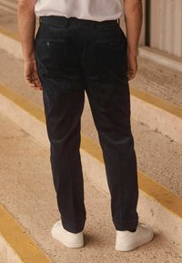 Navy corduroy-housut, joissa on kapeneva malli, kaksi takataskua napilla ja käänteet, yhdistettynä valkoisiin lenkkareihin.
