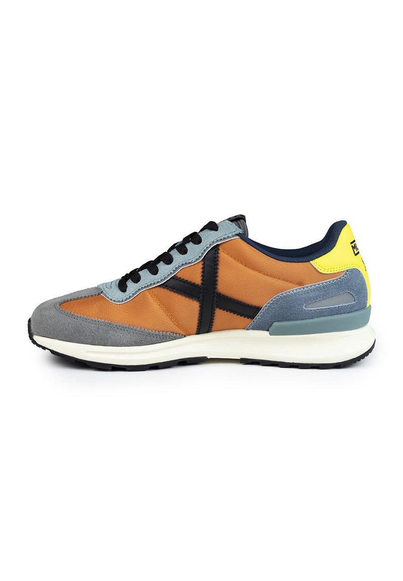 Sneaker som har en blandning av orange tyg och grå mocka, med svarta accenter, en vit mellansula och en gul detalj vid hälen. Svarta snörningar ingår.