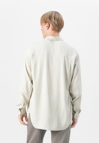 Helles beige Langarmhemd aus leichtem Stoff mit entspanntem Schnitt, abgerundetem Saum und Knopfmanschetten. Subtile Textur und klassisches Kragen Design.