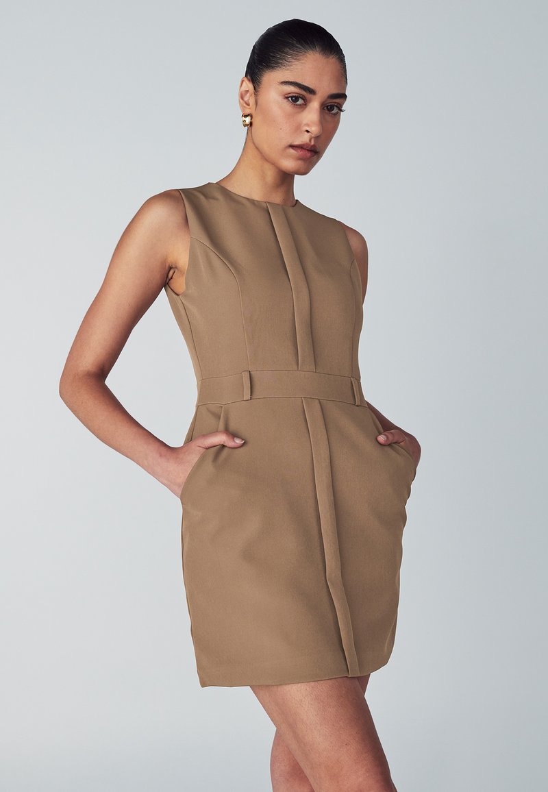 Tan mouwloze jurk met een gestructureerd ontwerp, zijkanten met zakken en een ceintuur in de taille. De stof lijkt glad met minimale stikdetails.