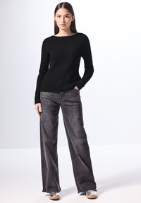 Maglione lungo a maniche lunghe nero a coste abbinato a jeans neri scoloriti a vita alta e gamba larga con orli sfrangiati. Le calzature presentano accenti metallici.