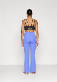 Μαύρο αθλητικό σουτιέν με πολλαπλές τιράντες και ανοίγματα, σε συνδυασμό με ανοιχτό μπλε κολάν με φαρδύ καμπάνα, που διαθέτει πλαϊνό άνοιγμα και μέση μεσαίου ύψους.