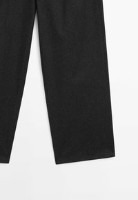 Partie inférieure d'un pantalon noir à jambe droite affichée sur un fond blanc, montrant la texture du tissu et les détails de l'ourlet.