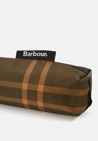 Peračník značky Barbour v tmavě zelené kostkované tkanině s hnědými pruhy, kulatého tvaru a odolným, strukturovaným povrchem.