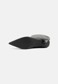 Black leather high-heeled shoe with a pointed toe and smooth texture. The sole is flat and slightly contoured, featuring minimal detailing.