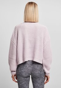 Lys rosa strikket genser med cropped snitt, ribbestrikkede mansjetter og detaljert tekstur. Kombinert med svarte mønstrete leggins.