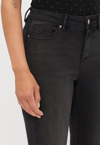 Černé džínové kalhoty mají slim fit, klasický pětikapsový design a hladkou texturu. Pas má poutka na opasek.