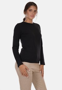 Maglietta nera a maniche lunghe con scollatura a girocollo e design aderente, realizzata in tessuto liscio. Indossata con pantaloni beige.