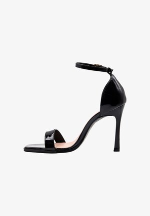Sandalo nero in pelle verniciata con tacco alto, cinturino alla caviglia, punta aperta e tacco a spillo su sfondo bianco.
