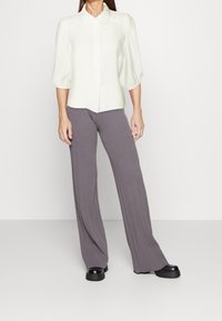 Light cream button-up shirt with puff sleeves, paired with wide-leg gray pants featuring vertical ribbing; solid black platform shoes.