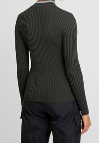 Donkergroene geribbelde top met lange mouwen, verticale strepen en een aansluitend ontwerp. Heeft een contrasterende witte kraag met een subtiele manchetdetail.