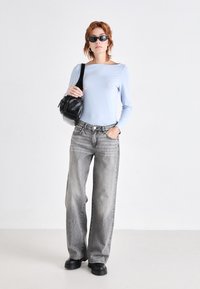 Lys blå langermet topp, grå vide jeans, svarte klumpete sko, og en liten svart håndveske. Modellen har på seg svarte ovale solbriller.