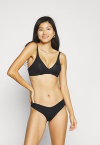 Ensemble de bikini noir avec un haut bralette décolleté et des bretelles fines, associé à un bas taille haute minimaliste. Tissu lisse sans motifs.