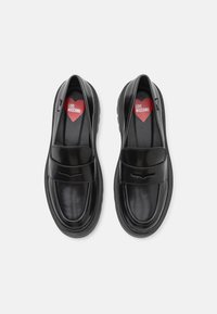 Zwarte loafers met een gladde leren afwerking, een ronde neus, subtiele stiksels en een lage rubberen zool. Voorzien van een rode hartinleg met "LOVE MOSCHINO."
