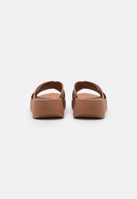 Sandali in gomma marrone con un design a fascia larga e una suola leggermente rialzata. La texture è liscia e il colore è uniforme in tutto il prodotto.