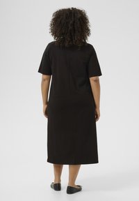 Abito midi in cotone nero con maniche corte, silhouette semplice, taglio dritto e cucitura centrale sul retro. Indossato con ballerine nere.